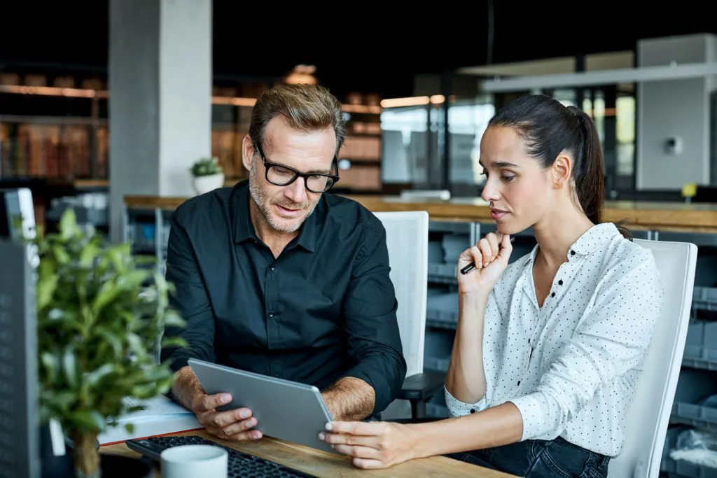 A male colleague showing information on a tablet to a female colleague in an office.