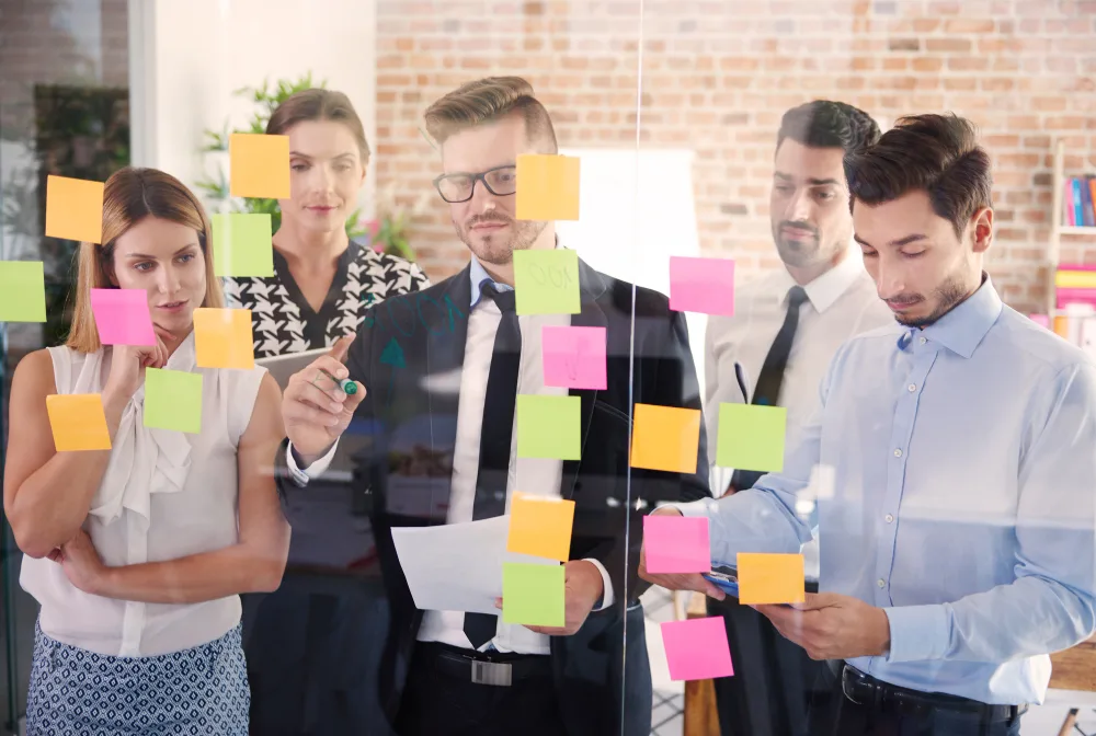A diverse team of professionals collaborating around a glass board covered with colorful sticky notes, symbolizing brainstorming and innovative ideas.