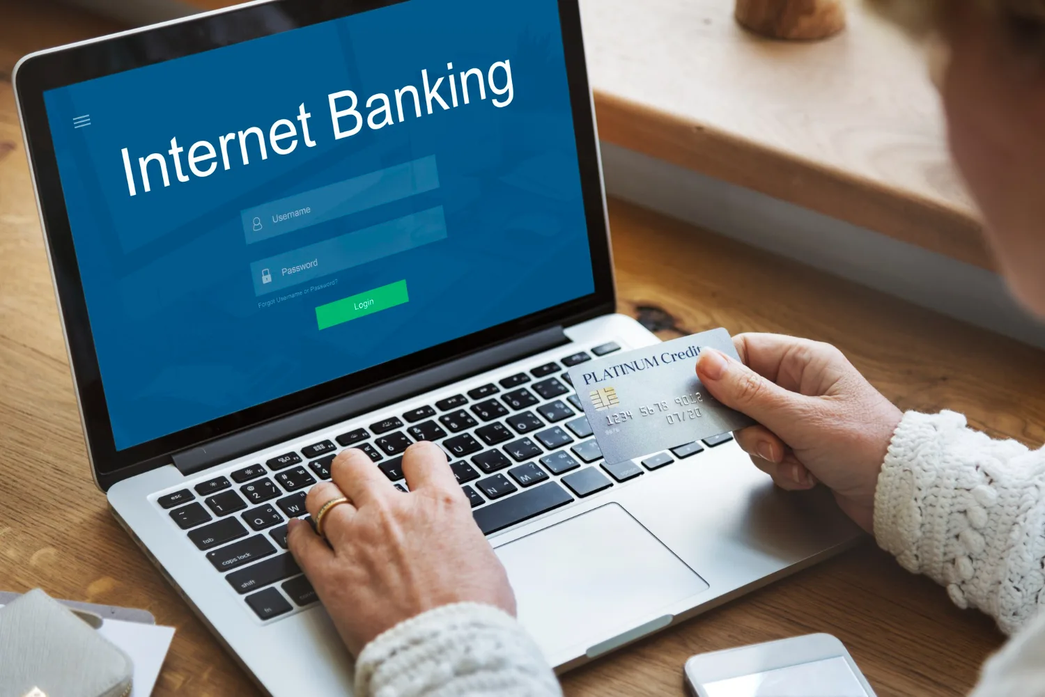 Businessman entering credentials into online internet banking site on laptop with card in a hand
