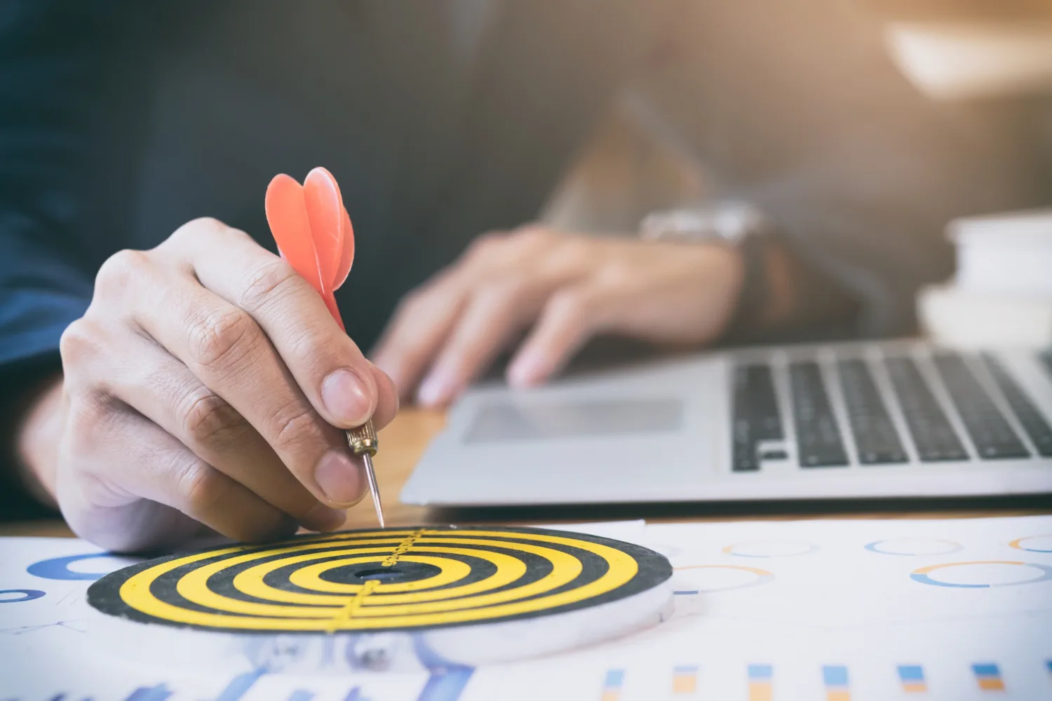 Man aiming dart at target board next to laptop, representing business goal alignment.